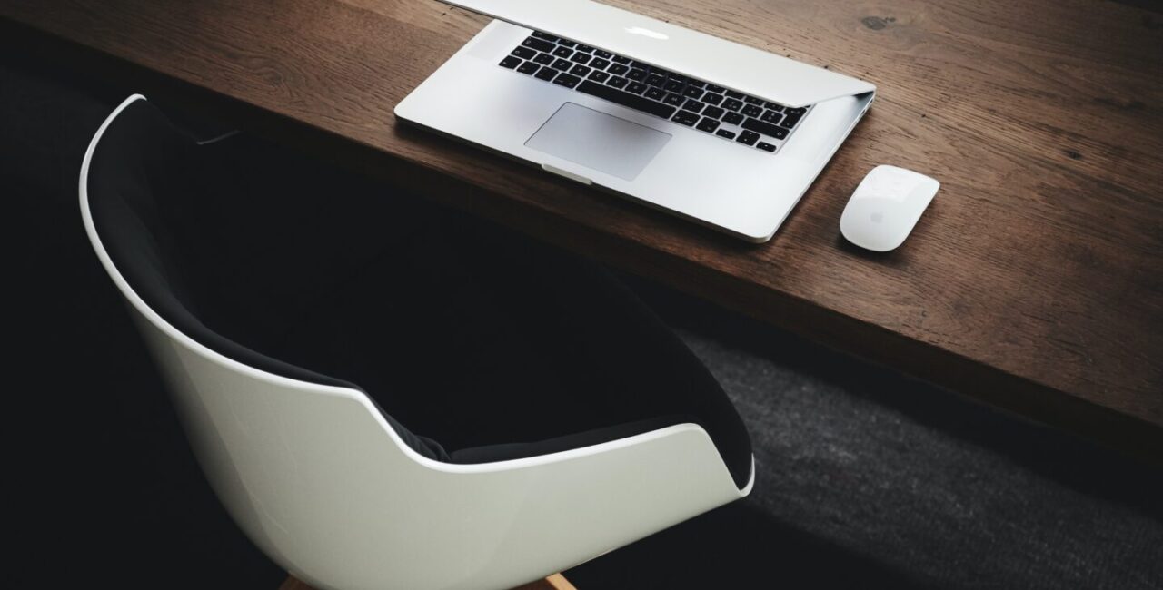 A white arm-chear, a white laptop on a wooden desk