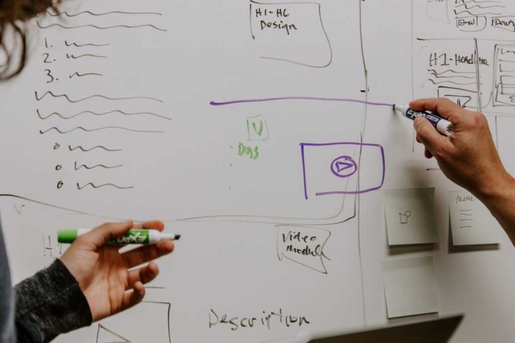Two people discuss a website design concept and draw it on a white board.