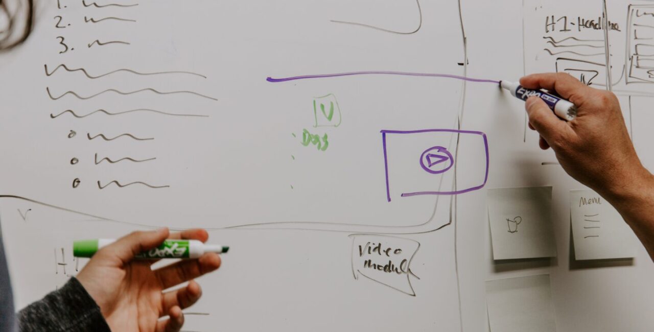 Two people discuss a website design concept and draw it on a white board.