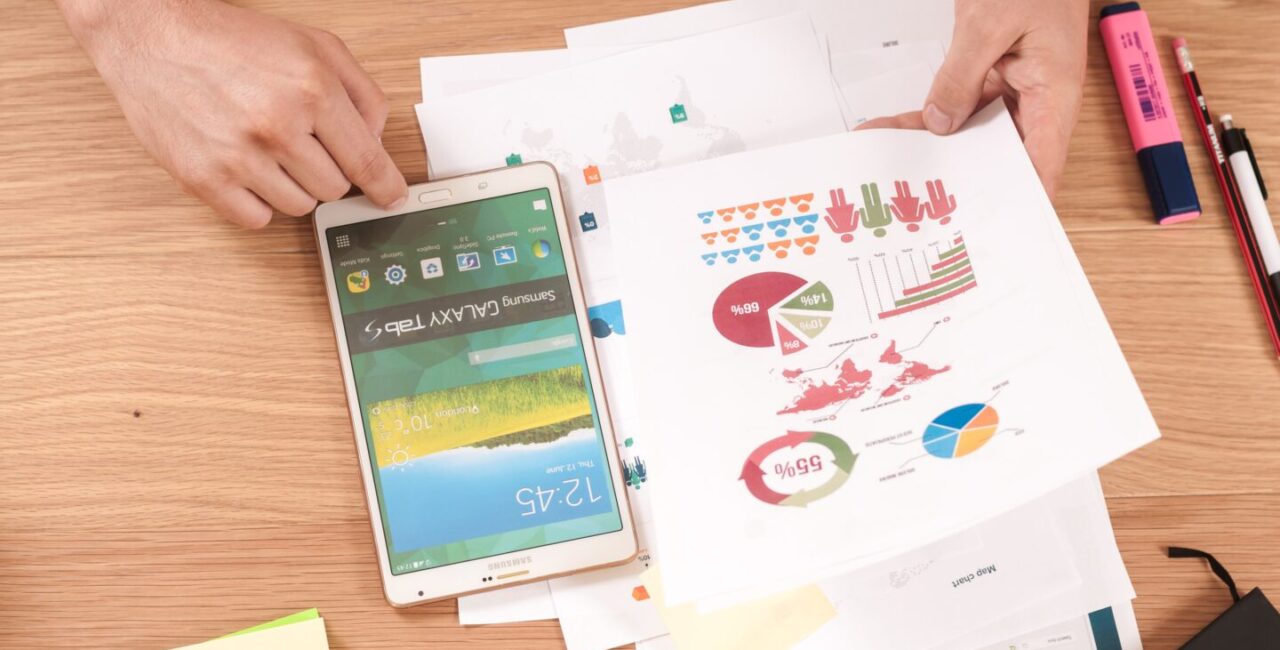 On white wood desk a planshet and papers with charts, diagrams that help to make decisions in digital marketing