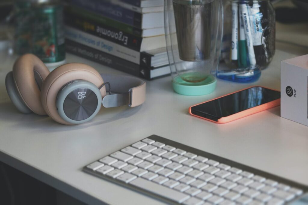 There are books about design, keyboard, headphones on the white table