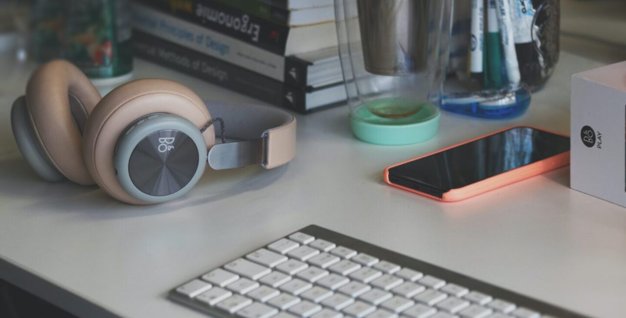 There are books about design, keyboard, headphones on the white table