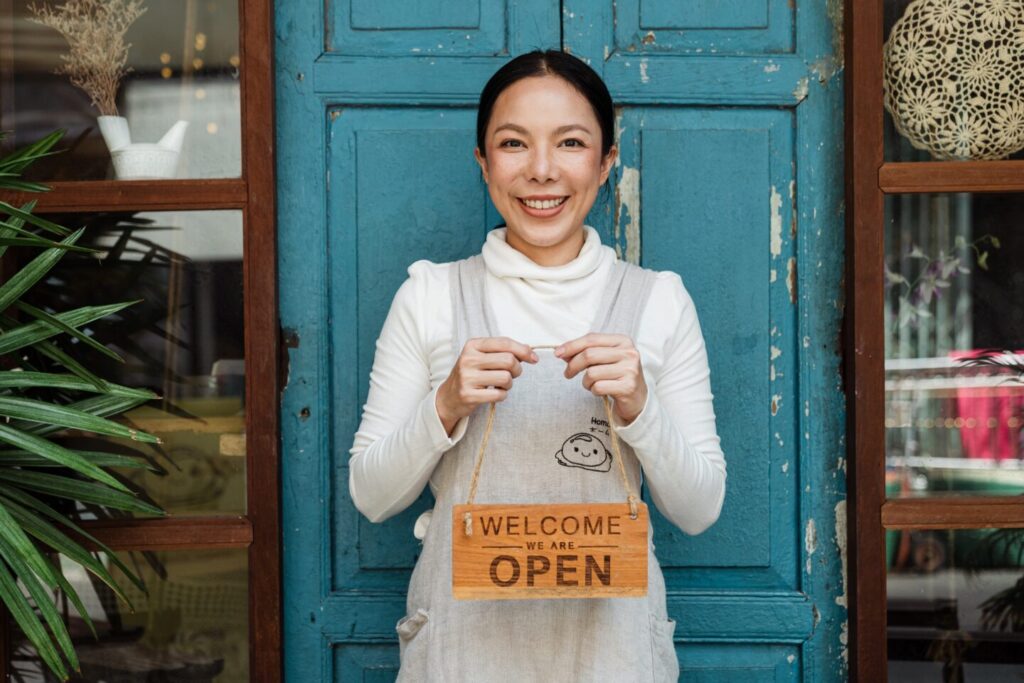 A woman is holding a sign Open, Welcome that means her business is opened.