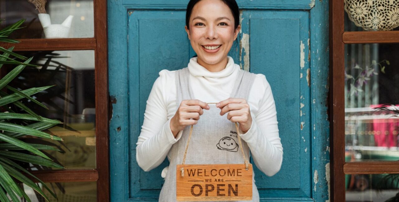 A woman is holding a sign Open, Welcome that means her business is opened.